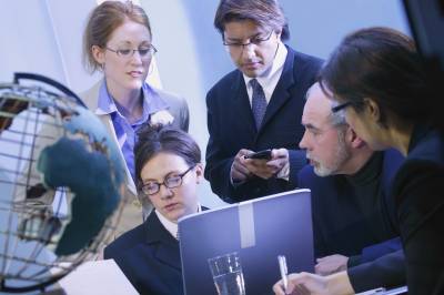 Business team discussing around laptop, globe visible, in a blue-toned photo.