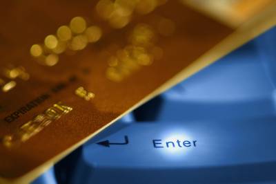Credit card above illuminated blue keyboard with "Enter" key, close-up photo.