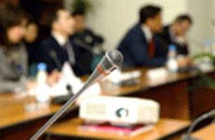 Microphone in focus at a conference table with blurred attendees, photo.