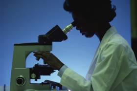 Scientist examines microscope, silhouette against blue background, photo, no visible text.