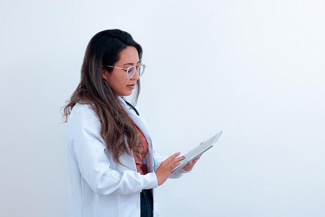 Woman in white coat using tablet, against plain white background, photo.