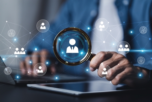 Person holding magnifying glass over digital icons, blue tones, photo style.