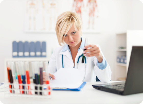 Doctor examining test tubes at desk, wearing white coat, in photo.