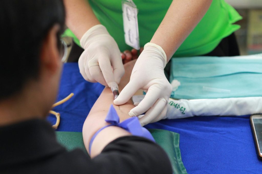 Healthcare worker drawing blood from patient's arm, wearing gloves, in photo.