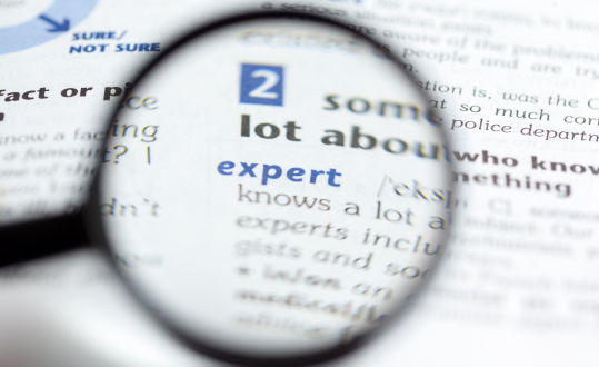 Magnifying glass highlighting "expert" in blue text on a printed page.