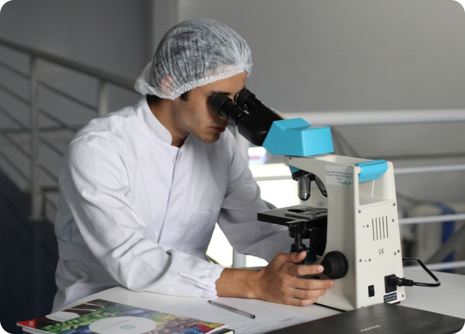 Scientist in white coat using microscope, blue accents, indoor laboratory photo.