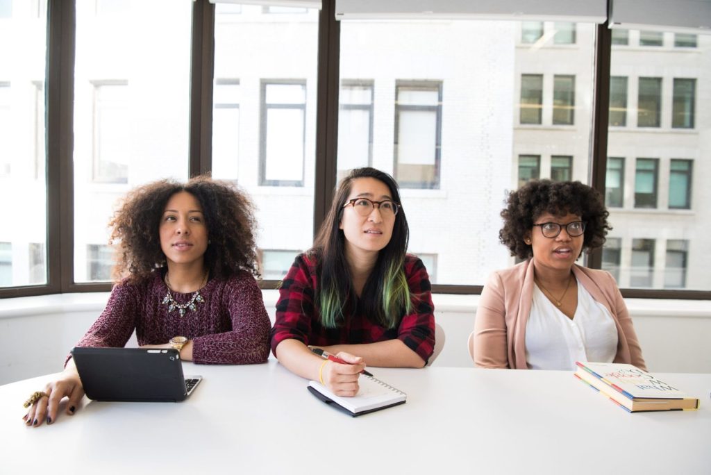 Three women attentively listening at a table, in a bright office photo.