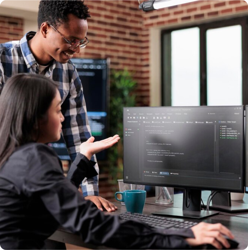 Two people collaborating at a computer, coding interface visible, in office.