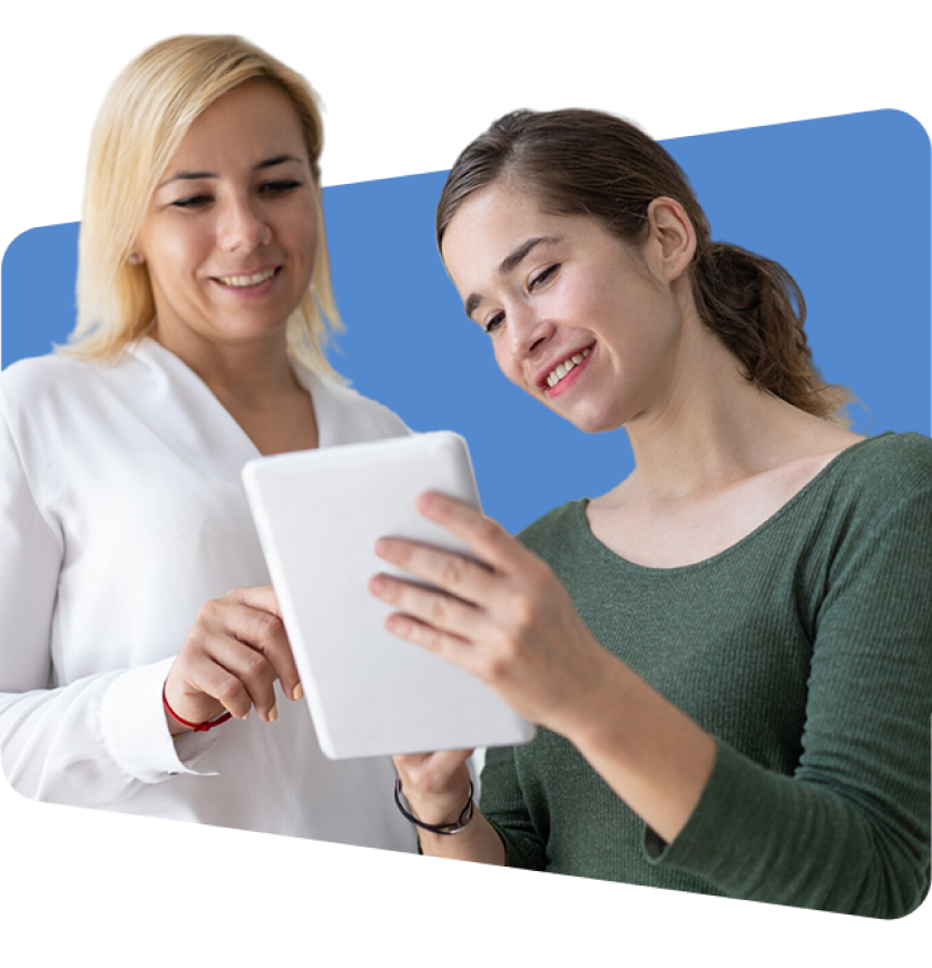Two women smiling at tablet, wearing white and green, against blue background.