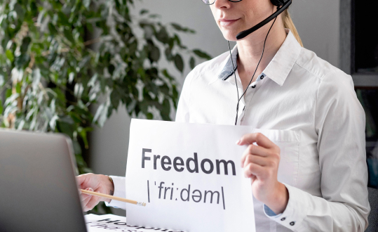 Woman holding "Freedom" sign, wearing headset, in white shirt, indoor photo.