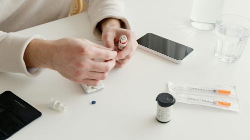 Person preparing medication with syringes on white table, photographed in color.