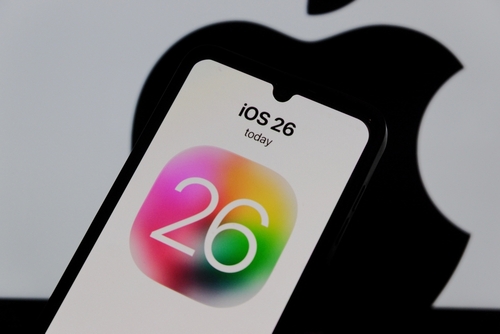 Smartphone displaying "iOS 26" with colorful icon, Apple logo in background.